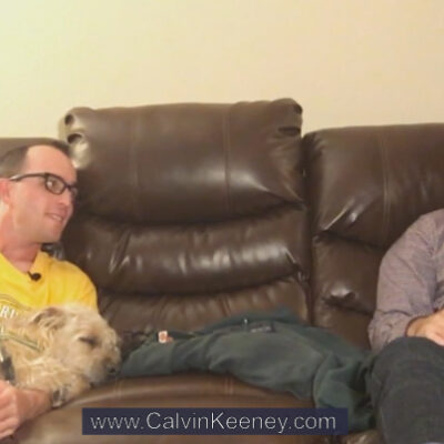 Calvin Keeney holding his dog named Nasus (terrier mix) on the couch while talking to Justen Aguillon who is also sitting on the couch