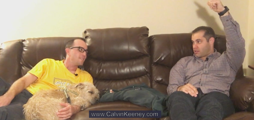 Calvin Keeney holding his dog named Nasus (terrier mix) on the couch while talking to Justen Aguillon who is also sitting on the couch