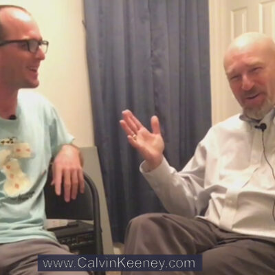 Calvin Keeney in a blue shirt looking at his uncle Rob Keeney as he explains photography to viewers on the camera