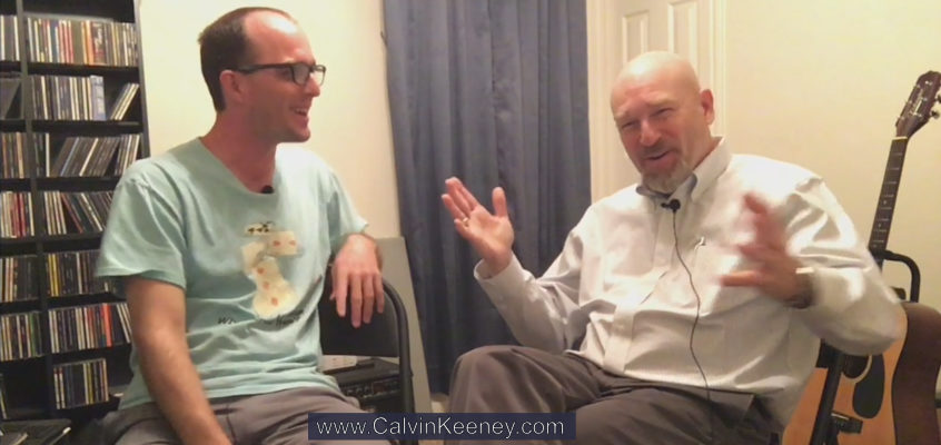 Calvin Keeney in a blue shirt looking at his uncle Rob Keeney as he explains photography to viewers on the camera