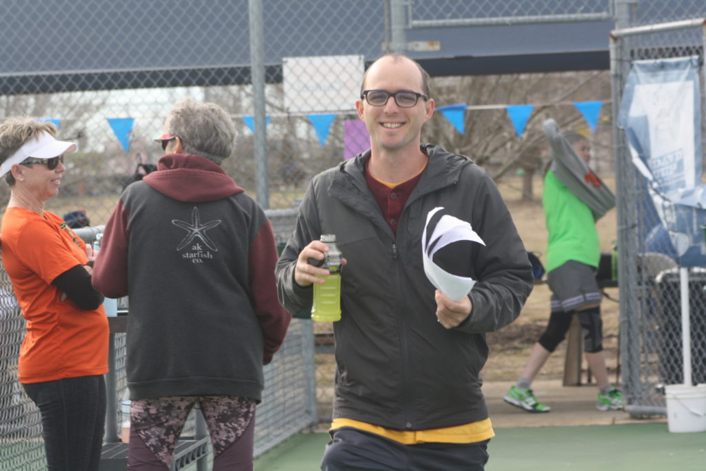 Calvin Keeney wearing a grey jacket and holding a yellow sports drink as he walks around the Pickleball courts hosting the New Years Eve Pickleball Tournament on December 31st, 2018