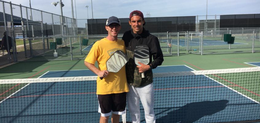 Calvin Keeney in a yellow shirt holding a Pickleball Paddle next to Tyson McGuffin in a black jacket holding a Pickleball Paddle