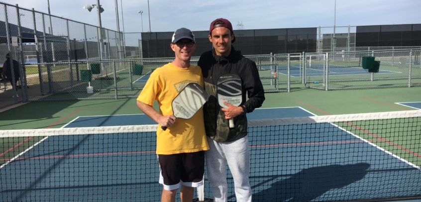 Calvin Keeney in a yellow shirt holding a Pickleball Paddle next to Tyson McGuffin in a black jacket holding a Pickleball Paddle