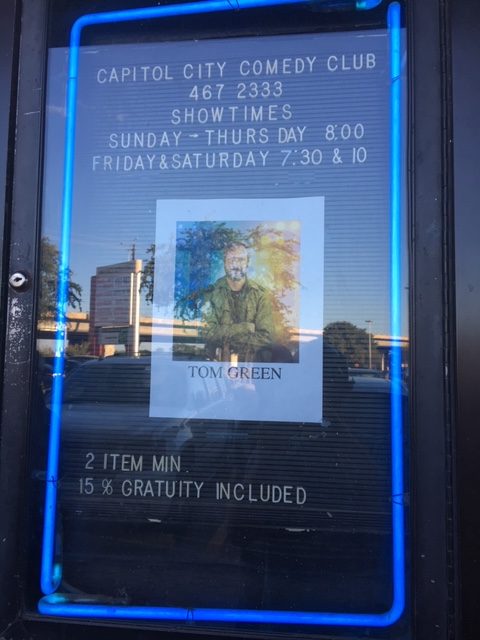 A flyer outside of Cap City Comedy Club in Austin, Texas for Tom Green. It mentions "Showtimes Sunday - Thursday 8pm. Friday and Saturday 7:30pm and 10pm"